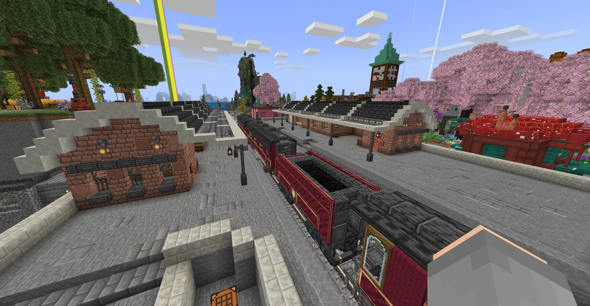 A red steam train stands at a brick station platform under cherry blossoms, with a clock tower behind.