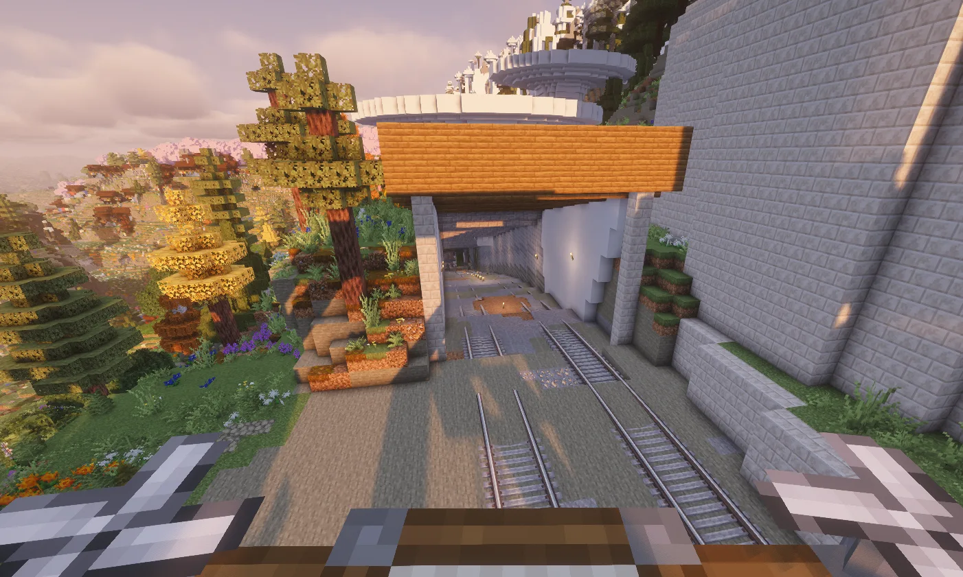 A quadrocopter view over Chisel Rock, with white rail structures, terraced gardens, snowy mountains, and a retro-futurist build in the distance.