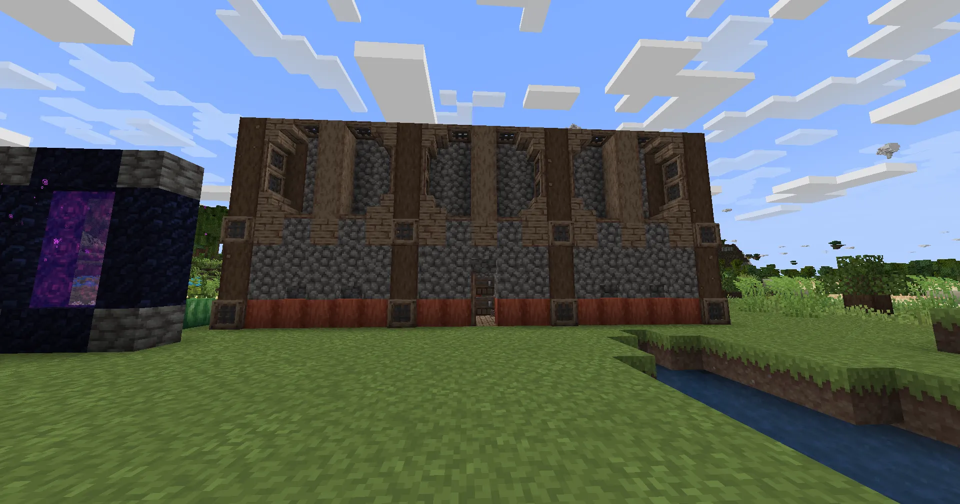 A timber-and-cobblestone house beside a glowing Nether portal under a bright sky.