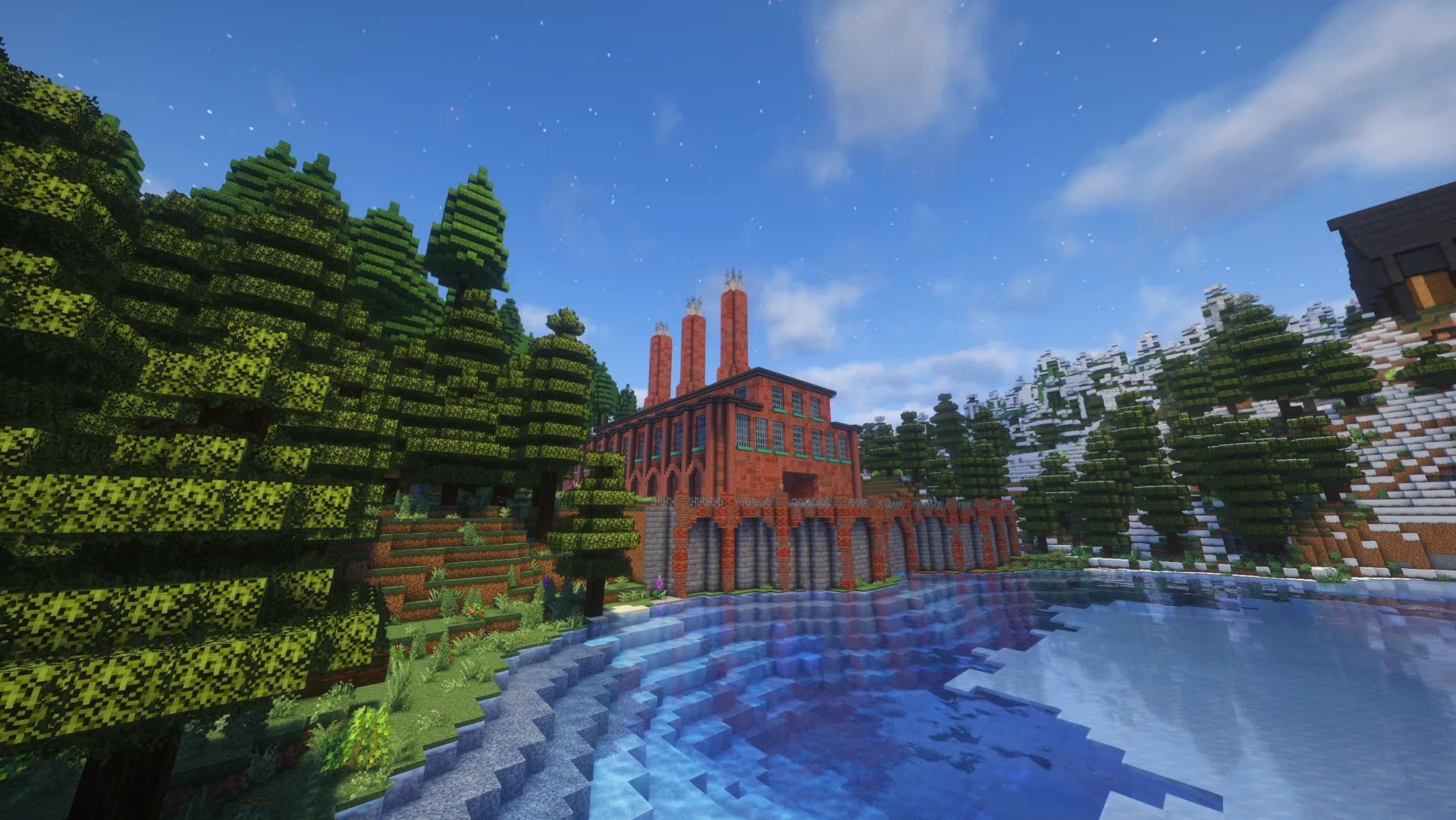 A red-brick industrial building with tall chimneys and arched lower bays beside a clear lake, framed by spruce forest and snowy hills.