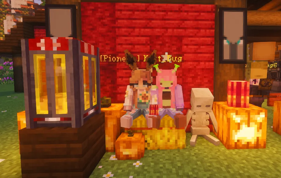 Two players sit together among carved pumpkins, glowing lanterns, and a small skeleton decoration outside a red-walled build.