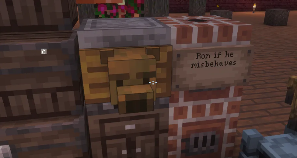 A carved wooden bear head mounted on a block beside a brick wall, next to a sign that reads "Ron if he misbehaves".