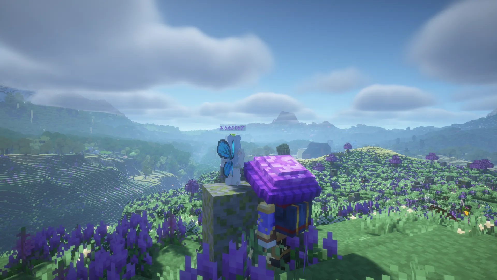 Two player characters beside a mossy block on a hillside covered in purple flowers, with wooded hills behind them.