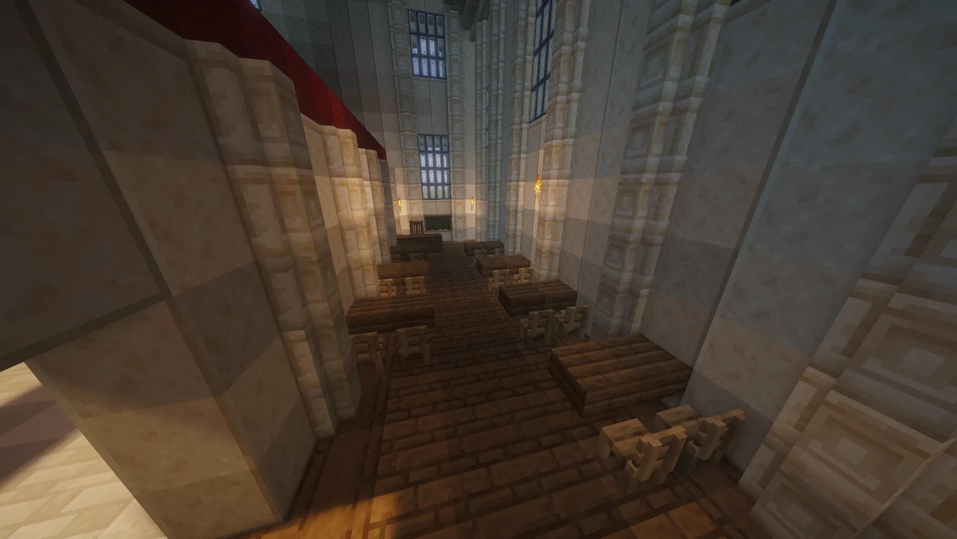 Rows of dark wooden desks and chairs in a tall stone classroom, with narrow windows, wall torches and a board at the far end.